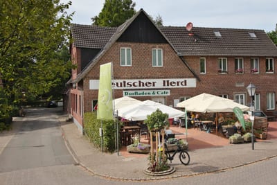 Der Dorfladen im Backsteinhaus „Deutscher Herd“, davor die Terrasse mit Sonnenschirmen und Gästen