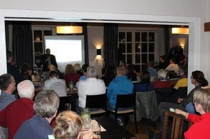 Ein Redner vor der Leinwand, davor das voll besetzte Publikum