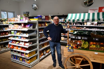 Geschäftsführer Johannes Wilp steht lächelnd im Verkaufsraum zwischen Süßwarenregal und Marktkarren mit Obst