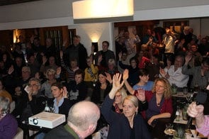 Viele Gäste im Saal heben die Hand