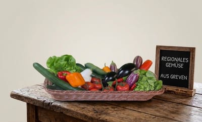 Korb mit Gemüse, daneben eine Tafel „Regionales Gemüse aus Greven“