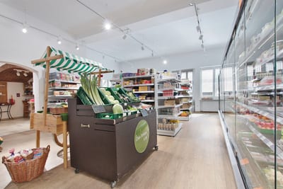 Verkaufsraum mit Gemüsestand, Regalen und langer Kühlregalwand